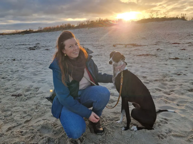 Bea Würriehausen kniet am Strand neben ihrem Hund im Sonnenuntergang